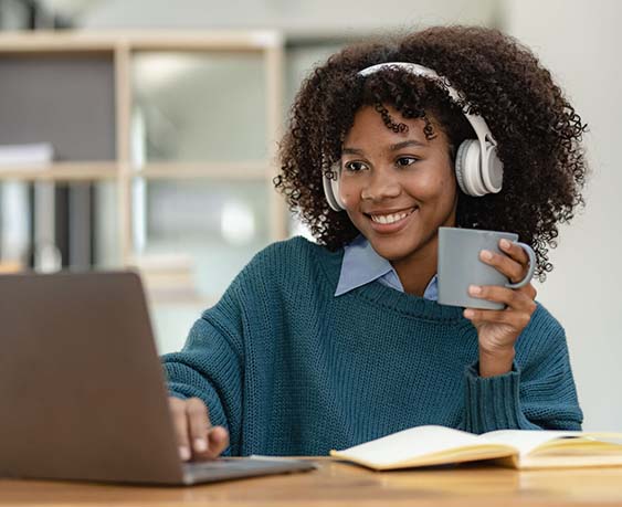 Young female student wearing headphones studying online training video communication Happy female student looking at computer screen, watching webinars or making video chat on webcam in library.