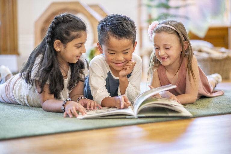 Friends reading a book together on the floor in the classroom.