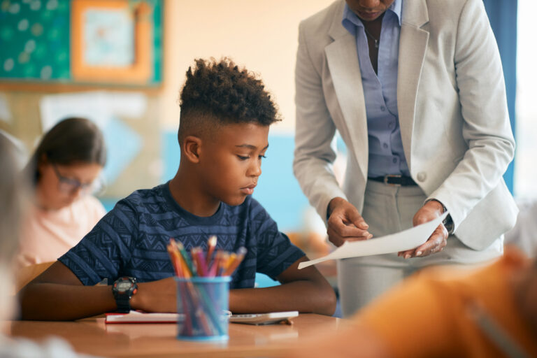 African American schoolboy studying with his teacher during a class at school.