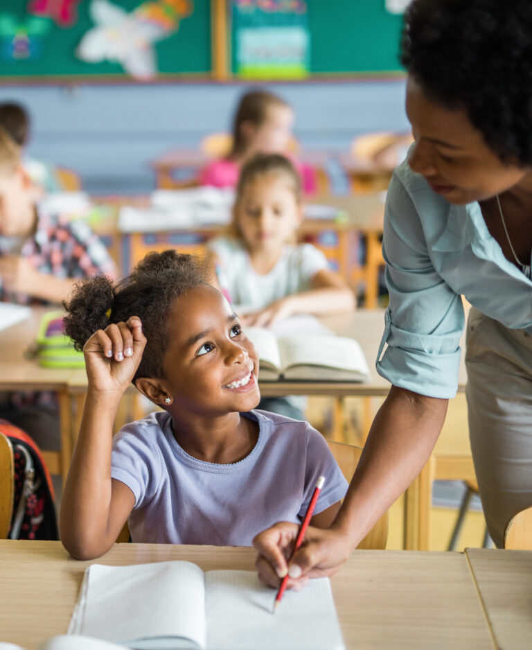 Happy African American girl having teacher's assistance during a class at elementary school.